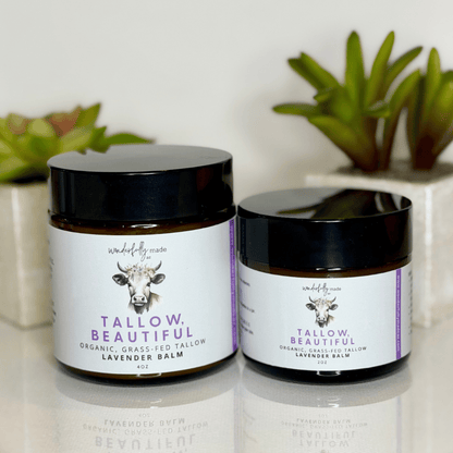 Two jars of Tallow Beautiful balm on a reflective surface with plants in the background.