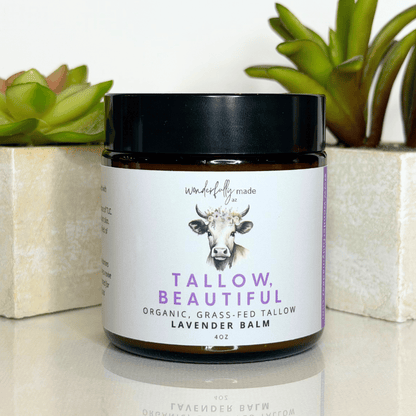 Jar of 'Tallow, Beautiful' lavender balm with a cow illustration on a white surface with plants in the background.