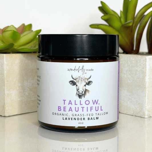 Jar of 'Tallow, Beautiful' lavender balm with a cow illustration on a white surface with plants in the background.