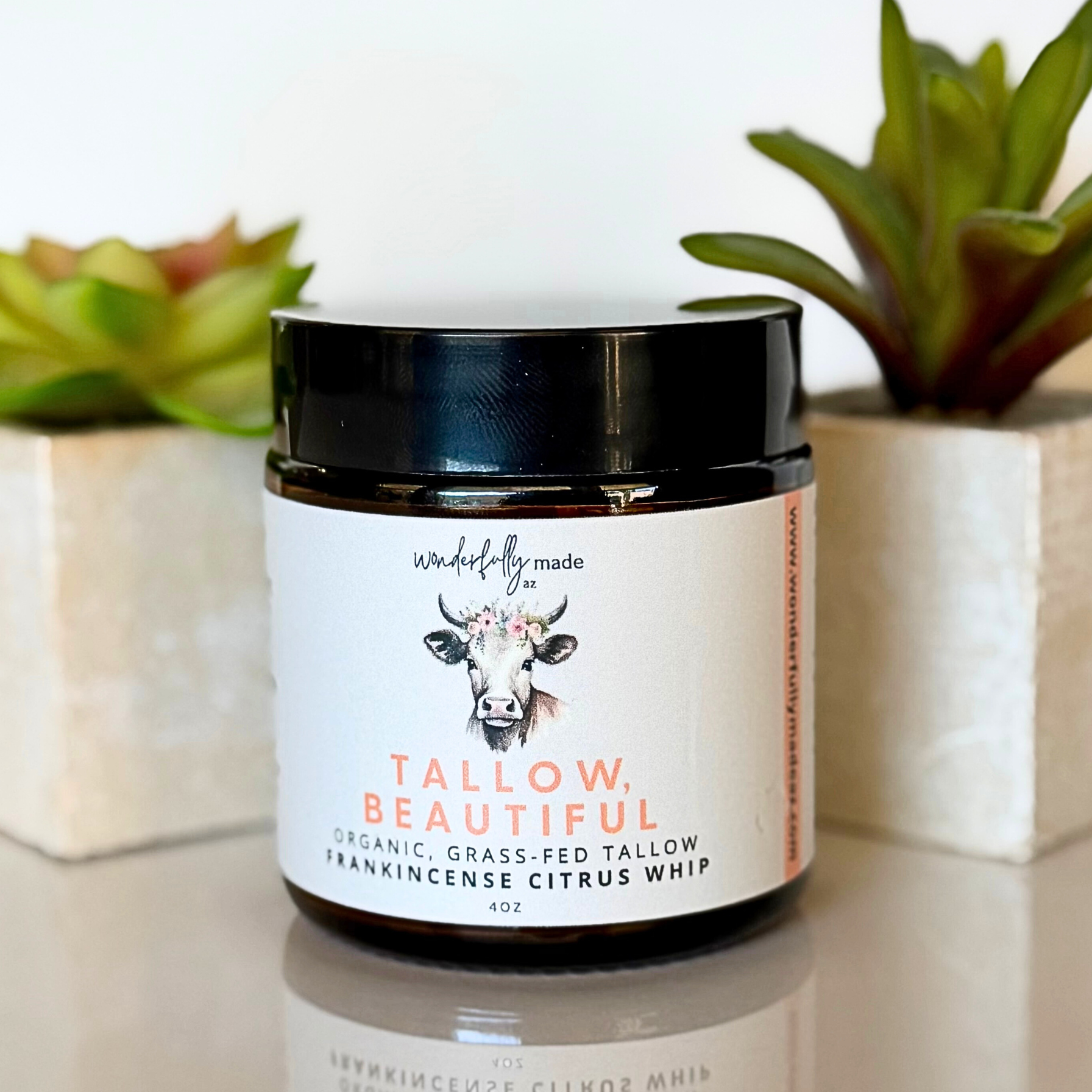 Jar of tallow product with a label featuring a cow illustration on a white surface with plants in the background.