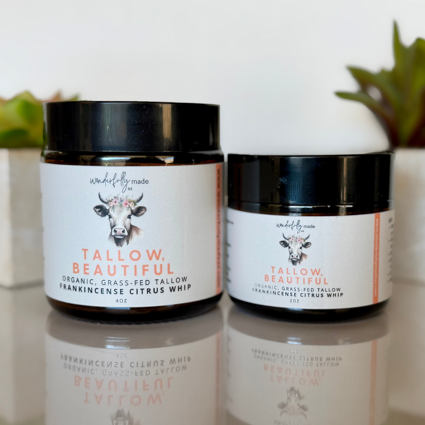 Two jars of Tallow Beautiful product on a reflective surface with a blurred background