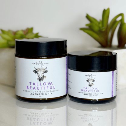 Two jars of 'Tallow Beautiful' product on a reflective surface with plants in the background.