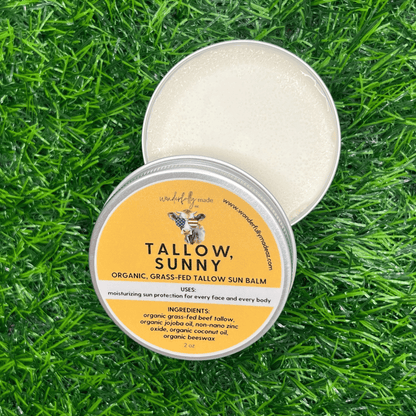 Tallow Sunny Sun Balm with open tin lid on grass